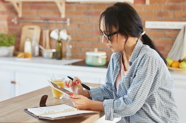 A close-up shot of a person writing in a meal planning notebook at a kitchen table, surrounded by cookbooks, fresh vegetables, and recipe cards, capturing the hands-on process of planning healthy meals.
