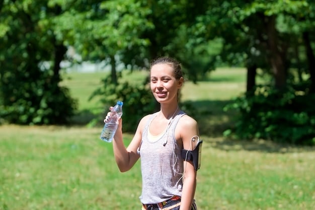 A person holding a reusable water bottle, exercising outdoors in a sunny park. The person is wearing athletic clothing, and there's a blurred background of trees and other people exercising.