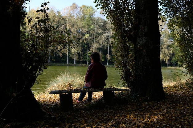A person sitting alone on a park bench looking thoughtful, with blurred figures of people passing by in the background.