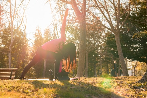 A person practicing yoga outdoors during sunrise, with a serene landscape in the background. The photo should convey a sense of peace, energy, and connection with nature, illustrating the benefits of physical activity and mindfulness.