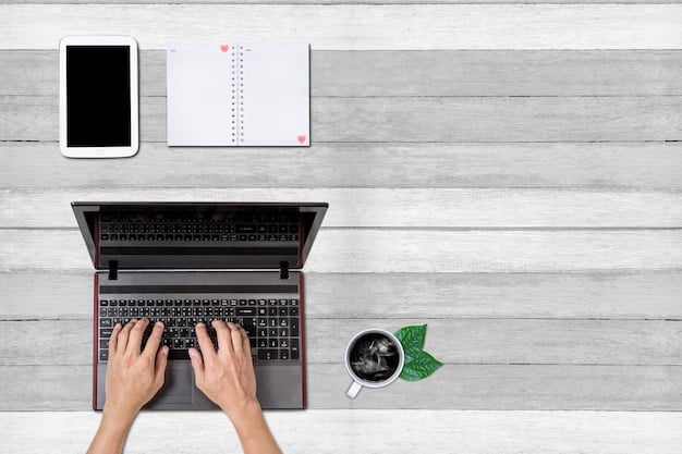 A top-down view of a neatly organized desk. A person's hands are visible, typing on a modern laptop with a spreadsheet open. To the side is a notebook with financial calculations, a pen, and a pair of glasses.