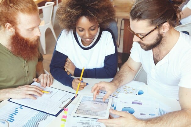 A diverse team of financial analysts brainstorming ideas around a table covered with charts and graphs in a brightly lit office, focusing on creating a detailed financial forecasting model for 2025.