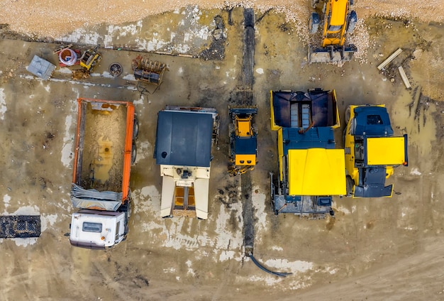 An aerial view of a construction site with various heavy machinery working on a new highway interchange. Workers in hard hats are visible, and the scene depicts busy construction activity under a clear blue sky.
