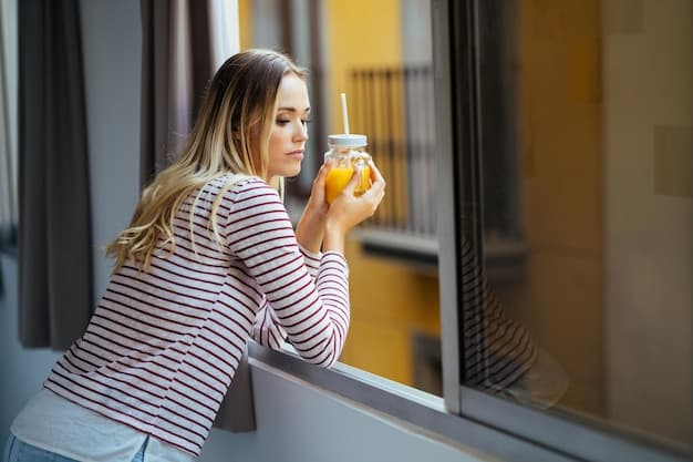 A person drinking a glass of orange juice next to a window with snow falling outside, illustrating the importance of vitamin C and a healthy diet during winter.