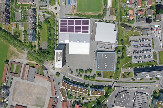 An aerial view of a modern office building with solar panels on the roof. The building is surrounded by green landscaping, and the image emphasizes sustainability and environmental responsibility. The sky is clear and blue, and the overall impression is one of innovation and forward-thinking.